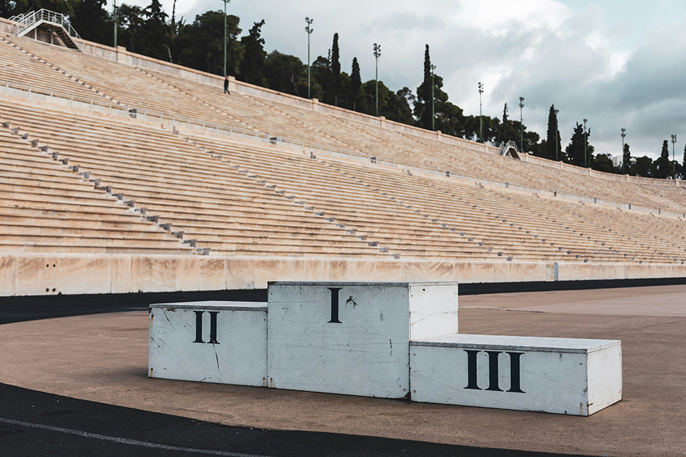 An empty stadium with a stage carrying the steps for 1st, 2nd, and 3rd place, indicating how signaling eliteness motivates manager participation